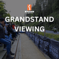 An image depicting a group of people seated in a grandstand area, watching a motorcycle race. The grandstand is labeled with 'GRANDSTAND VIEWING' and the logo of 'THE BLACK DUB'.